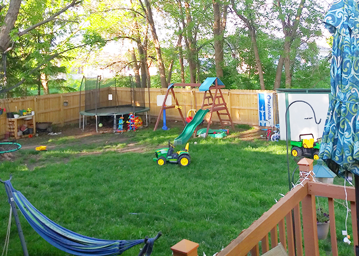 Photo of Kyler's backyard with a trampoline, a swing set, and toys all encompassed by a privacy fence.